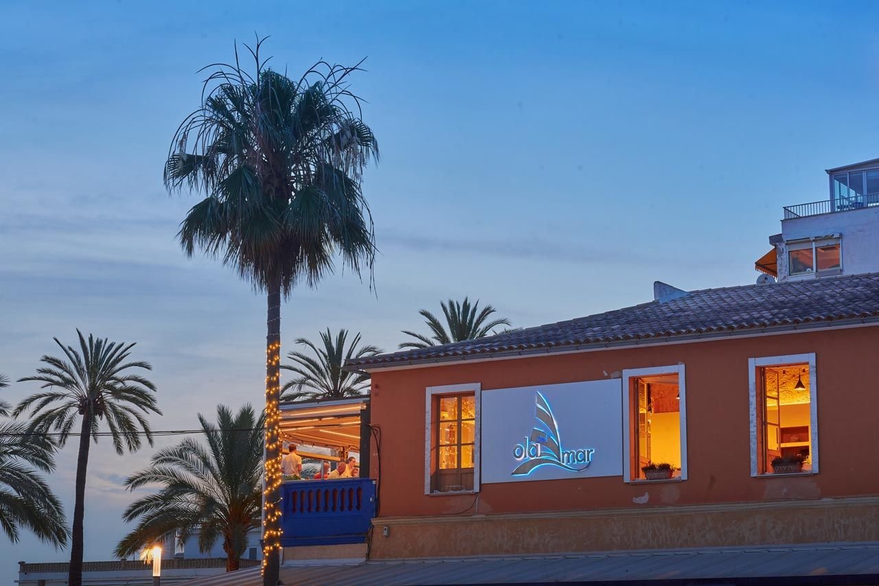 Fachada de Ola del Mar a la hora azul, palmeras y ventanas iluminadas