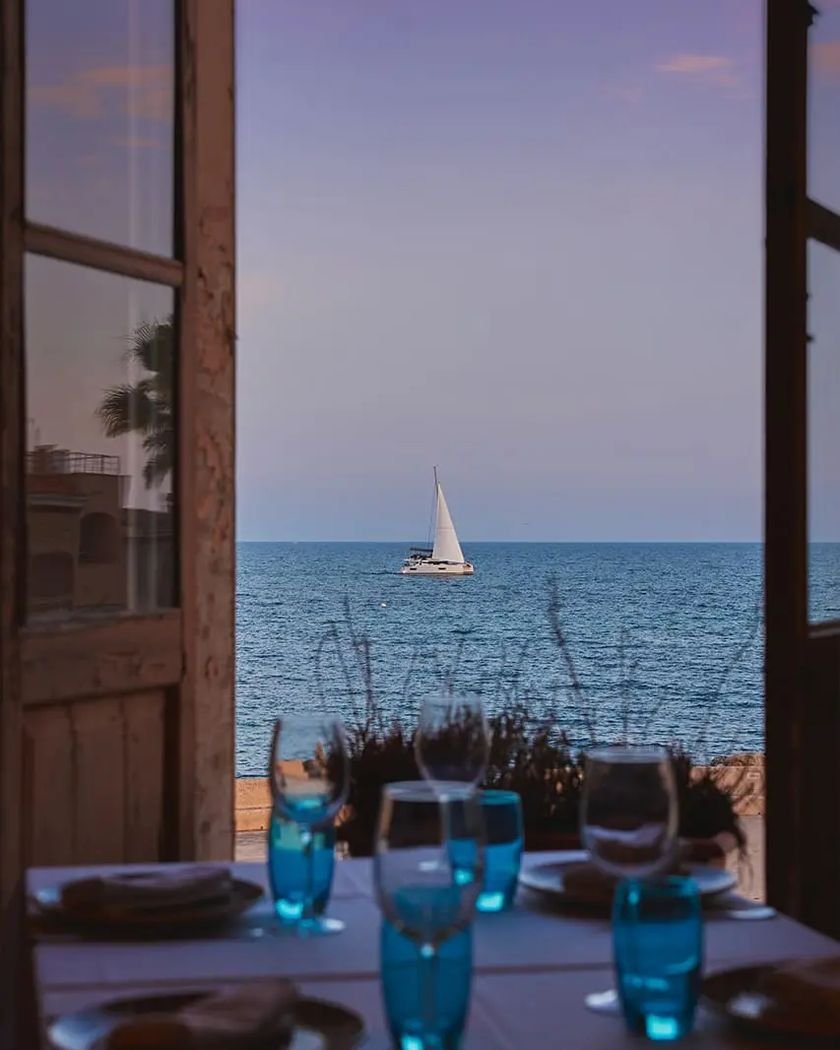 El mar y un velero vistos desde la puerta abierta del restaurante