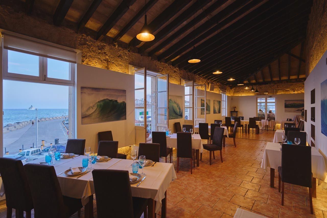 Comedor con mesas puestas y ventanas hacia el mar
